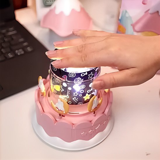 Main d’un adulte allumant une veilleuse bébé rose avec projections lumineuses et décor lune.